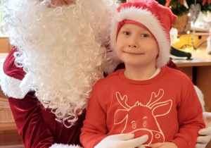 Chłopiec pozuje do zdjęcia z Mikołajem i prezentem