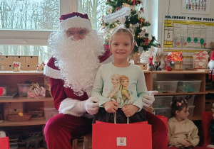Dziewczynka pozuje do zdjęcia z Mikołajem i prezentem