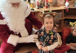 Chłopiec pozuje do zdjęcia z Mikołajem i prezentem