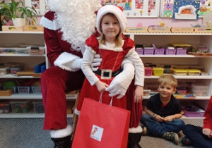 Dziewczynka pozuje do zdjęcia z Mikołajem i prezentem
