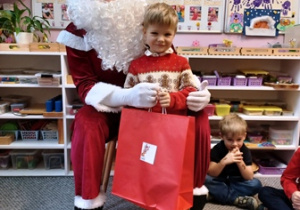 Chłopiec pozuje do zdjęcia z Mikołajem i prezentem