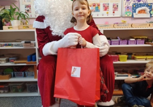 Dziewczynka pozuje do zdjęcia z Mikołajem i prezentem