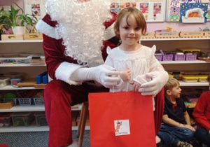 Dziewczynka pozuje do zdjęcia z Mikołajem i prezentem