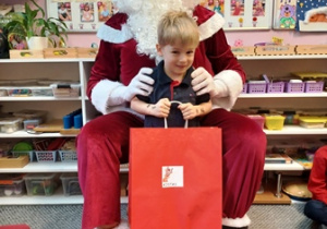 Chłopiec pozuje do zdjęcia z Mikołajem i prezentem