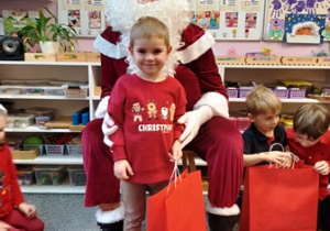 Chłopiec pozuje do zdjęcia z Mikołajem i prezentem