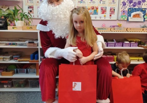 Dziewczynka pozuje do zdjęcia z Mikołajem i prezentem