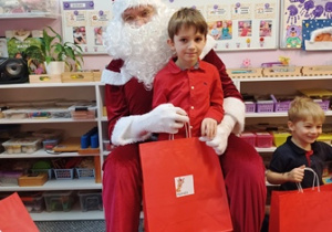 Chłopiec pozuje do zdjęcia z Mikołajem i prezentem