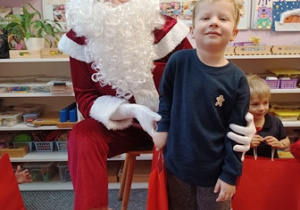 Chłopiec pozuje do zdjęcia z Mikołajem i prezentem