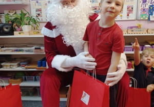 Chłopiec pozuje do zdjęcia z Mikołajem i prezentem