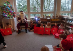 Dzieci siedzą w kręgu z prezentami i kolędują z Mikołajem.