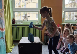 Dziewczynka podnosi do góry kubeczek ustawiony na stoliku