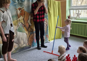 Aktorzy stoją na scenie wraz z dziewczynką, która trzyma w ręku grabie