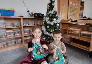 Tosia i Ignaś pozują do pamiątkowego zdjęcia przy choince ze świątecznym upominkiem przygotowanym dla Rodziców