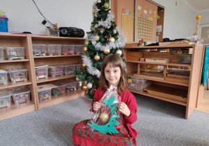 Dziewczynka pozuje do pamiątkowego zdjęcia przy choince ze świątecznym upominkiem przygotowanym dla Rodziców