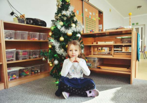 Dziewczynka pozuje do pamiątkowego zdjęcia siedząc przy choince