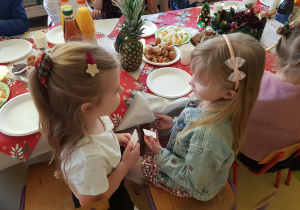 Dziewczynki siedzą przy stole i dzielą się opłatkiem