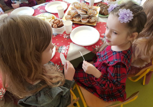 Dziewczynki siedzą przy stole i dzielą się opłatkiem