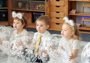 Dzieci podczas tańca siedzą na białym materiale i trzymają w rękach balony z motywem śnieżynek