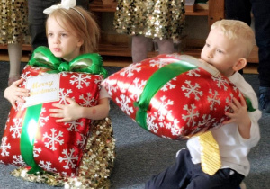 Chłopiec i dziewczynka podczas tańca, siedzą na dywanie i trzymają w dłoniach balony w kształcie prezentów