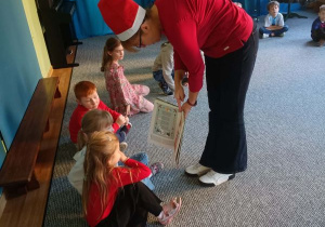 Dzieci siedzą w kręgu i oglądają obrazki w książce pokazywane przez prowadzącą warsztaty