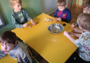 Chłopcy siedzą przy stoliku i jedzą suszone jabłka