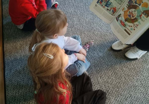 Dzieci siedzą w kręgu i oglądają obrazki w książce pokazywane przez prowadzącą warsztaty