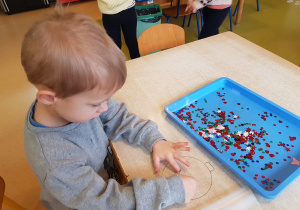 Chłopiec wykonuje bombkę z wykorzystaniem cekinów