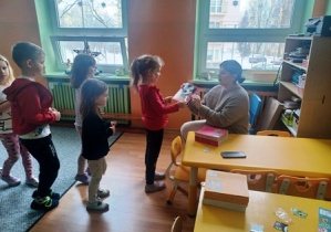 Dzieci podchodzą do prowadzącej i wymieniają kupony na książki