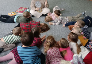 Dzieci leżą na dywanie i słuchają opowieści o pieniądzach prowadzącej zajęcia
