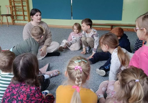 Dzieci siedzą w kręgu i słuchają opowieści prowadzącej zajęcia