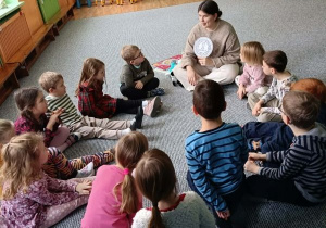 Dzieci siedzą w kręgu i słuchają opowieści prowadzącej zajęcia