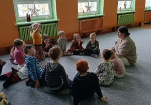 Dzieci siedzą w kręgu i słuchają opowieści prowadzącej zajęcia