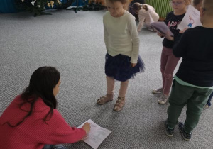 Dzieci stoją ustawione w kolejce i podchodzą do pani po pieczątkę