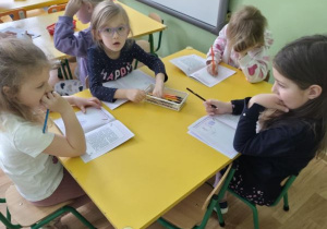 Dzieci siedzą przy stolikach i rysują w książeczkach