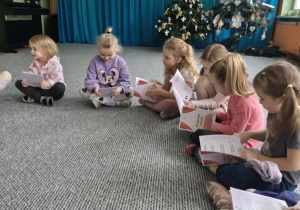 Dzieci siedzą w kręgu i oglądają książeczki