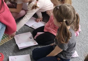 Dzieci siedzą na dywanie z książeczkami