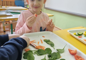 Dziewczynka siedzi i je plasterek marchewki