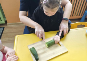 Dziewczynka kroi ogórka z pomocą pani dietetyk