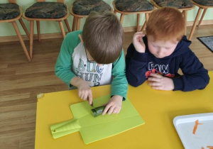 Chłopiec kroi ogórka, drugi chłopiec siedzi obok i przygląda się