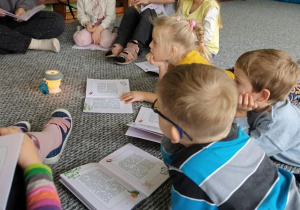 Dzieci siedzą i leżą na dywanie, oglądając książeczki