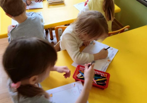 Dzieci siedzą przy stolikach i rysują w książeczkach