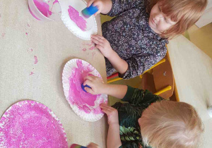 Dzieci stemplują papierowe talerzyki różową farbą