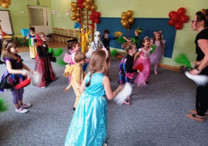 Dzieci przebrane w stroje karnawałowe tańczą trzymając w dłoniach kolorowe pompony