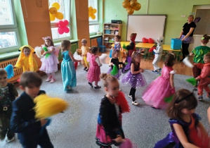 Dzieci przebrane w stroje karnawałowe tańczą trzymając w dłoniach kolorowe pompony