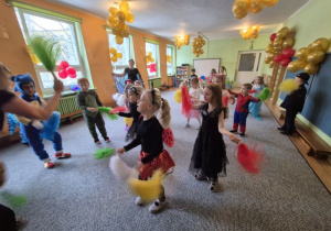 Dzieci przebrane w stroje karnawałowe tańczą trzymając w dłoniach kolorowe pompony