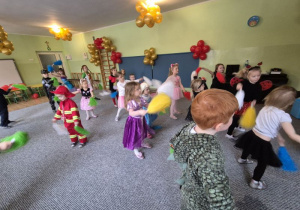 Dzieci przebrane w stroje karnawałowe tańczą trzymając w dłoniach kolorowe pompony