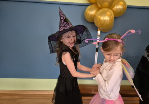 Dziewczynka w stroju czarownicy tańczy z dziewczynką w stroju motylka