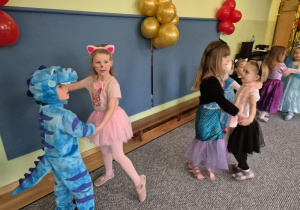 Dziewczynka w stroju kotka tańczy z chłopcem w stroju dinozaura, obok tańczą dwie dziewczynki (przebrane za syrenkę i kotka)