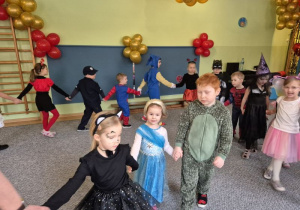 Dzieci w strojach karnawałowych trzymają się za ręce tworząc długiego węża