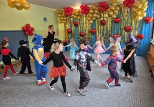 Dzieci w strojach karnawałowych trzymają się za ręce tworząc długiego węża